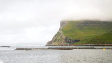 Faroe Adaları 'ndaki Atlantik Okyanusu' nda bir balık çiftliğinin yanındaki teknede balık avlamak. Sisin içinde saklı tepeler. Yüksek kalite 4k görüntü.