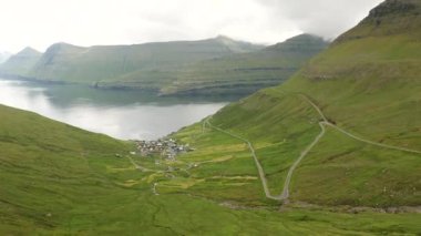 Faroe Adaları 'ndaki Kalsoy Adası' ndaki Trollanes köyüne giden dolambaçlı bir yol manzarası. Muhteşem Faroe doğası, yeşil tepeler ve güzel kayalıklar ve dağlar. Kalsoy Adası 'ndan Kunoy' a manzara.