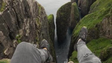 4K Güzel Dunnesdrangar manzarası, Faroe Adaları. Erkek bacakları Vagar, Faroe Adaları 'ndaki uçurumdan sarkıyor. Bacak Adam Uçurumun kenarında oturuyor. İnanılmaz doğa, büyük kayalıklar ve dağlar..