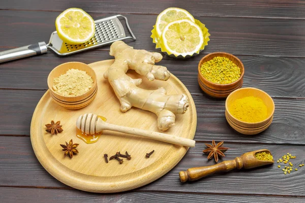 Ginger root and dry ginger powder in bowl on board. Lemon wedges, spices and dry turmeric. Dark wooden background. Top view