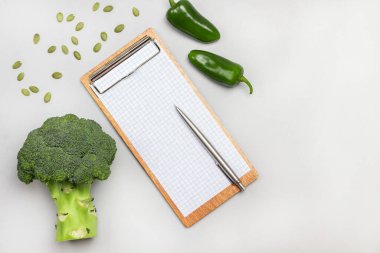 Boş kâğıt ve kalemle dolu bir pano. Brokoli, yeşil biber ve tohum. Düz yatıyordu. Uzayı kopyala Gri arkaplan