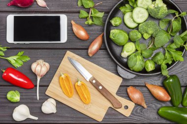 Boş kâğıt ve kalemle dolu bir pano. Masada çok renkli sebzeler var. Gri arka plan. Düz yatıyordu. Boşluğu kopyala