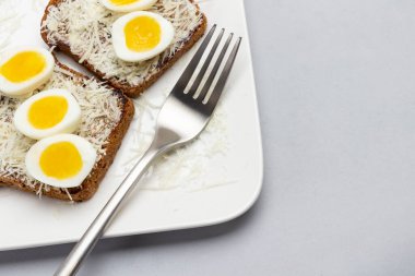 Rendelenmiş peynirli tost, haşlanmış bıldırcın yumurtası, beyaz tabakta çatal. Uzayı kopyala Gri arka plan. Üst görünüm