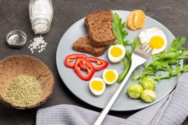 Çatal ve sahanda yumurta, Brüksel lahanası, doğranmış kırmızı biber ve yarım haşlanmış yumurta. Kuru baharat ve tuz. Gri peçete. Siyah arka plan. Üst görünüm.