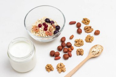 Fındık, tahta kaşıkta yulaf ezmesi. Böğürtlen ve mısır gevreği kasede. Kavanozda yoğurt. Beyaz arka plan. Üst görünüm