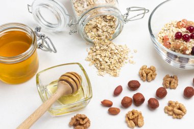 Kasede bal çubuğu. Fındıklar masada. Cam kavanozda yulaf ezmesi ve bal. Beyaz arka plan. Üst görünüm