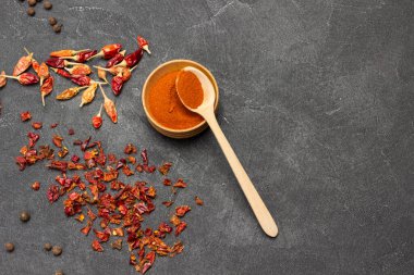 Tahta kâse ve kaşıkta kırmızı biber. Masada kırmızı biber ve kuru biber yaprakları var. Uzayı kopyala Siyah arka plan. Düz yatıyordu