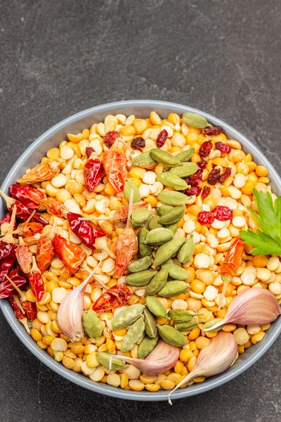 Cardamom, garlic, onion and dry pepper pods on peas in bowl. Copy space. Black background. Flat lay