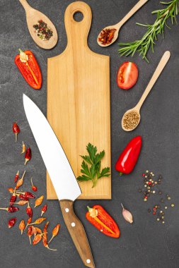 Kesme tahtasındaki mutfak bıçağı. Kırmızı biberler, kuru kabuklar ve biber yaprakları masada. Tahta kaşıklarda kuru biber. Düz yatıyordu. Siyah arkaplan