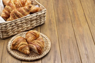 Fresh croissants in wicker basket and plate. Copy space. Top view. Wooden background.