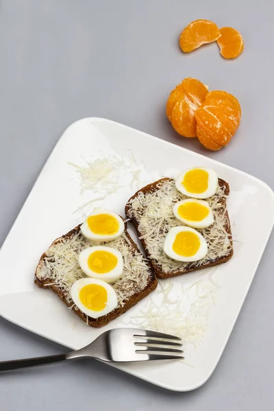 煎蛋和烤奶酪三明治 叉子放在白盘上 桌子上有剥皮的橘子 顶部视图 灰色背景 — 图库照片