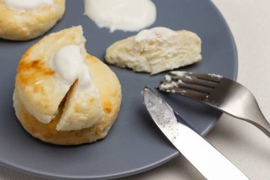 Ekşi kremalı, çatallı ve bıçaklı peynirli kekler gri tabakta. Üst Manzara. Beyaz arkaplan