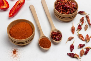 Ahşap kâse ve kaşıkta öğütülmüş biber. Masada kuru biber kabukları var. Üst Manzara. Beyaz arkaplan