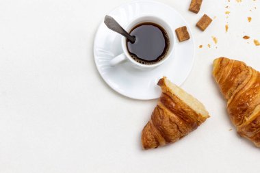 Masada iki parça kruvasan var. Bir fincan kahve ve tahıl. Uzayı kopyala Düz yatıyordu. Beyaz arkaplan.