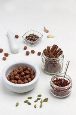 Masanın üzerinde fındıklar var. Allspice kasede. Cam kavanozlarda tarçın çubukları ve kuru biber yaprakları. Uzayı kopyala Beyaz arka plan. Üst görünüm