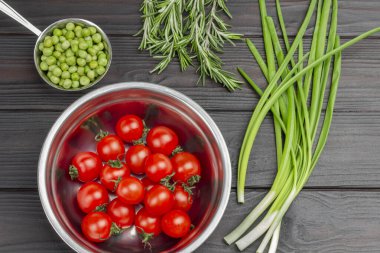 Domatesler ve metal kaselerde taze bezelyeler. Yeşil soğan ve biberiye. Düz yatıyordu. Koyu tahta arkaplan