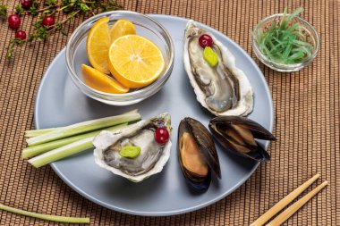 Açık midye ve istiridye kabukları, gri tabakta bir kase limon. Üst Manzara. Tahta sopalardan peçete..