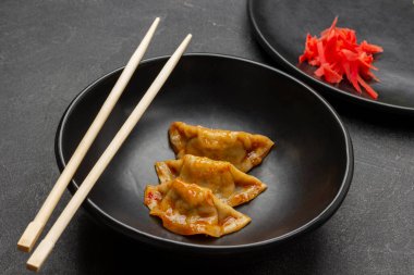 Siyah kasede üç gyoza köftesi ve çubuk yemek. Siyah kasede zencefil turşusu. Üst Manzara. Siyah arkaplan