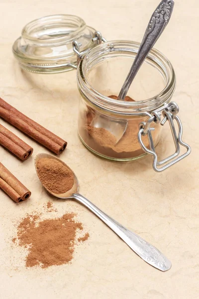 Yer tarçını metal kaşıkta ve masada. Cam kavanozda tarçın ve kaşık. Üst Manzara. Kahverengi arkaplan.
