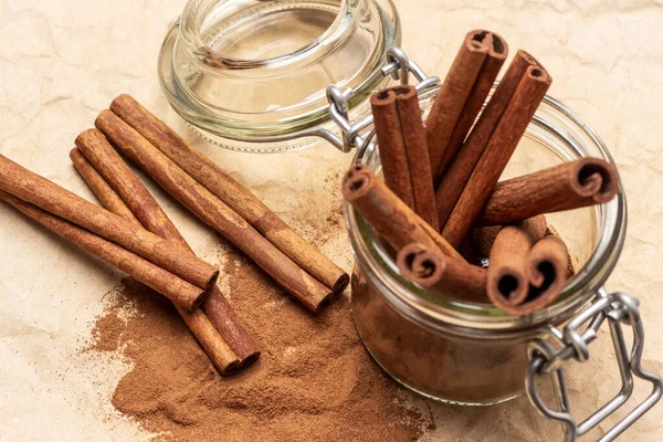 Cam kavanozda tarçın çubukları. Tarçın çubukları, tarçın ve masa. Düz yatıyordu. Kahverengi arkaplan.