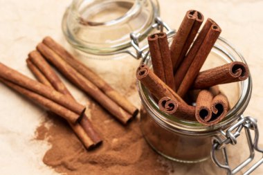 Cam kavanozda tarçın çubukları. Tarçın çubukları, tarçın ve masa. Düz yatıyordu. Kahverengi arkaplan.