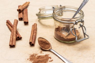 Yerdeki tarçın kaşıkta ve cam kavanozda. Tarçın çubukları masada. Üst Manzara. Kahverengi arkaplan.