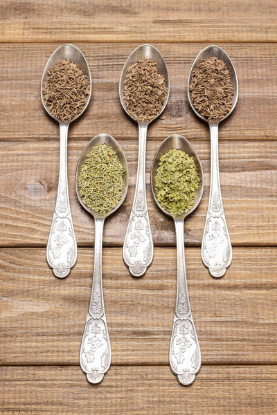 Fennel seeds and dry herbal spices and  in metal spoons. Top view. Wooden background