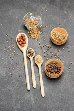 Kişniş çekirdeği, cam kavanozda tüm baharatlar ve ahşap kaseler. Kaşıklar içinde fındık ve baharat tohumları. Kişniş tohumları masaya saçılmış. Düz yatıyordu. Siyah arkaplan.