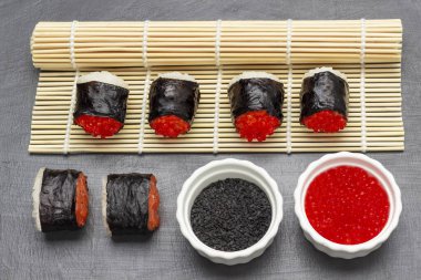 Suşi nori havyarlı ve somonlu bambu hasırı ve masada. Siyah susam ve beyaz kaselerde havyar. Üst Manzara. Gri arkaplan.