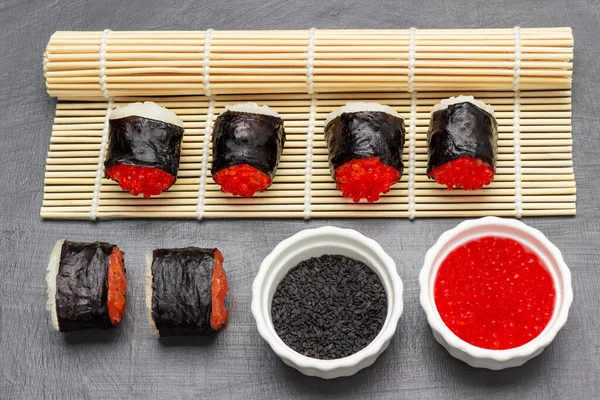 Suşi nori havyarlı ve somonlu bambu hasırı ve masada. Siyah susam ve beyaz kaselerde havyar. Üst Manzara. Gri arkaplan.