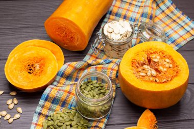 Cam kavanozlarda kabak çekirdeği. Peçetede yarı balkabağı ve dilimlenmiş balkabağı parçaları. Üst Manzara. Koyu tahta arkaplan.