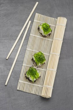 Bambu hasırında yosun suşisi. Yemek çubukları masada. Düz yatıyordu. Gri arkaplan.
