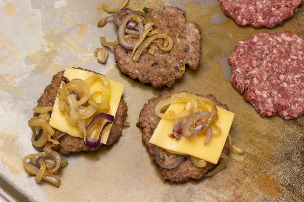 Fried burgers with cheese and onions. Raw burgers on a rusty metal background. Top view