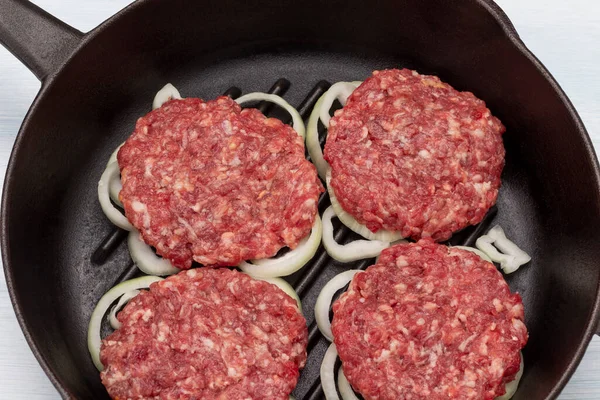 Raw burgers with onions in a frying pan. Flat lay