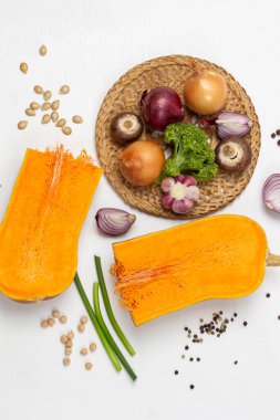 Hasır tabakta soğan, mantar, tuzluk ve lahana. Masada iki balkabağı ve yeşil saplar var. Düz yatıyordu. Beyaz arkaplan.