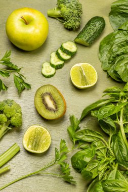 Lime and kiwi halves, apple, green basil sprigs and chopped cucumber. Flat lay. Green background.
