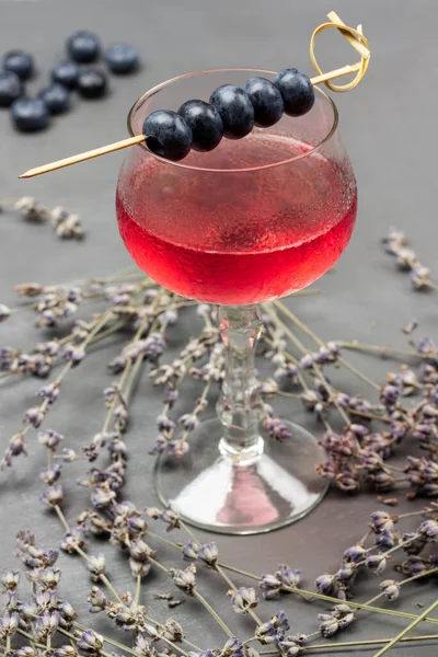 Blueberries on skewer. Wine glass with cooling drink. Drops of water on misted glass of wine glass. Sprigs of lavender on table. Top view. Grey background
