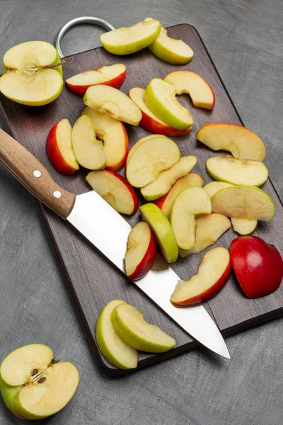 Halves a green apple. Slices of green and red apples and kitchen knife on cutting board. Flat lay. Grey background