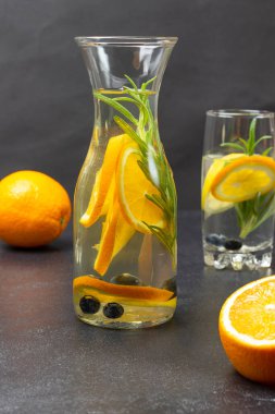 Infused summer drink with oranges, blueberries and rosemary in bottle. Orange on table. Black background
