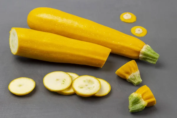 Whole zucchini and sliced yellow zucchini. Top view. Grey background.