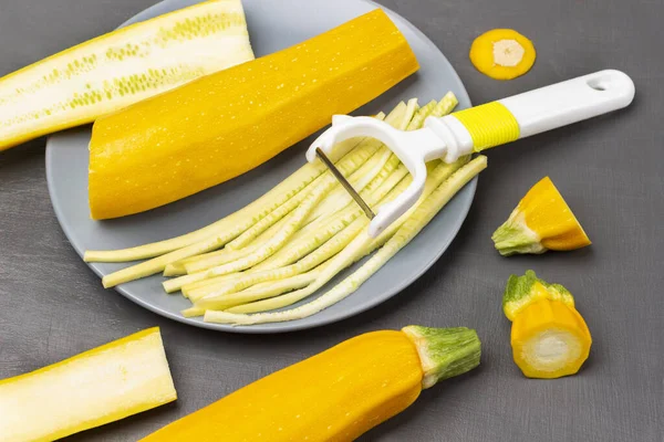 Striped yellow zucchini, zucchini halves and vegetable cutter on gray plate. Yellow zucchini on table. Flat lay. Grey background