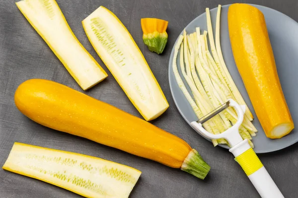 Yellow zucchini on table. Striped yellow zucchini, zucchini halves and vegetable cutter on gray plate.  Flat lay. Grey background