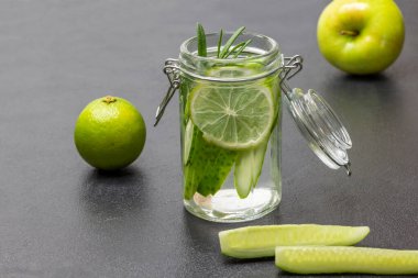 Limonlu yaz içeceği ve kavanozda salatalık. Salatalık dilimleri masada. Masada limon ve elma. Siyah arkaplan.
