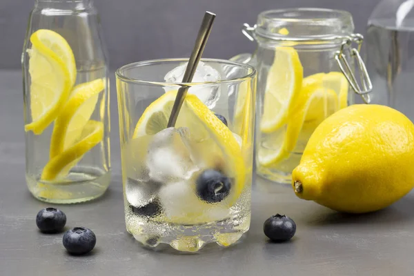 Misted glass with ice and lemon. Whole lemon and blueberries on table. Close up. Grey background