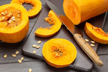 Bıçak, balkabağı dilimleri kesme tahtasında. Masanın üzerinde yarım bir balkabağı. Üst Manzara. Koyu tahta arkaplan.