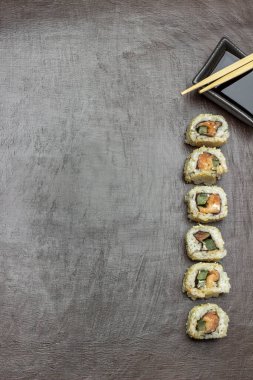 Suşi arka arkaya dizilir. Soya sosu ve yemek çubuğuyla bir kase. Uzayı kopyala Düz yatıyordu. Kahverengi arkaplan.