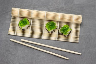 Bambu hasırında yosun suşisi. Yemek çubukları masada. Düz yatıyordu. Gri arkaplan