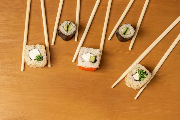 Chopsticks hold sushi. Flat lay. Copy space. Mustard color background.