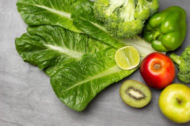 Marul, brokoli ve biber, kivi ve limon dilimleri, masada elmalar. Düz yatıyordu. Yeşil arkaplan.