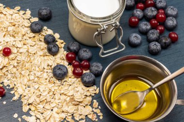 Yulaf ezmesi, yabanmersini ve yabanmersini. Kavanozda yoğurt, metal kasede bal. Üst Manzara. Mavi arkaplan.